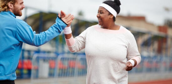 Happy woman giving high five to her personal trainer while running on track