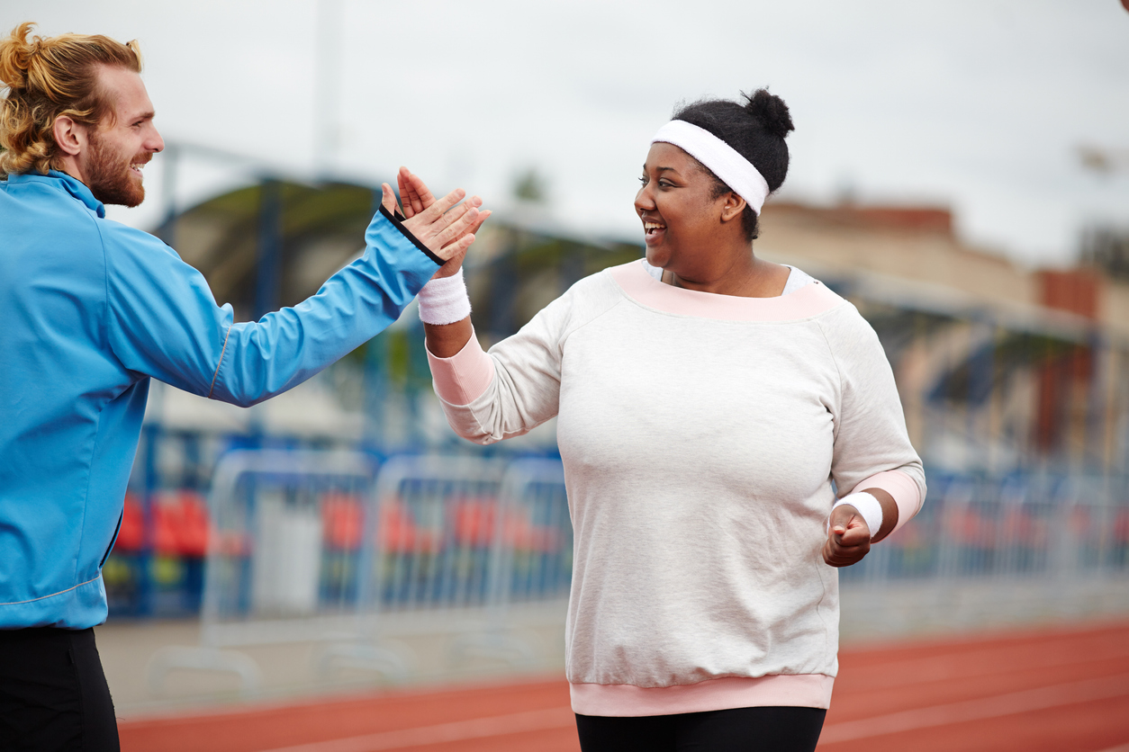 Happy woman giving high five to her personal trainer while running on track
